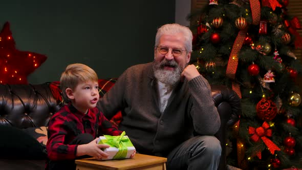 Little Boy in a Festive Red Plaid Shirt is Shake Gift Box in Anticipation of Surprise