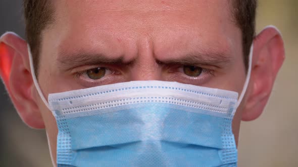 Man in Protective Face Mask Looks at Smartphone Holding It in Hands on Street