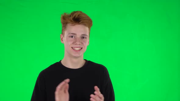 Portrait of Ginger Teenager Boy with a Tattoo Is Having Fun and Clapping His Hands on a Green Screen