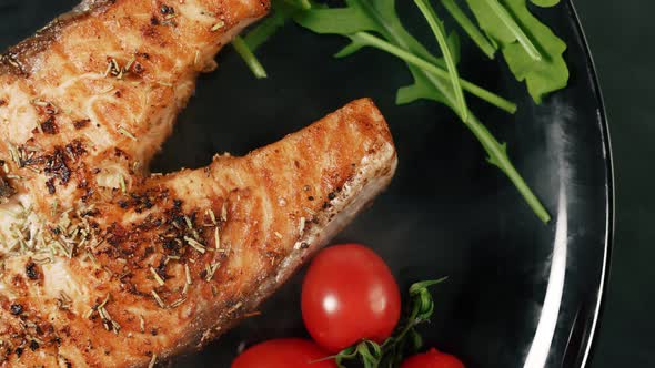 A Cooked Salmon Steak with the Addition of Aromatic Spices and Vegetables on a Black Serving Plate