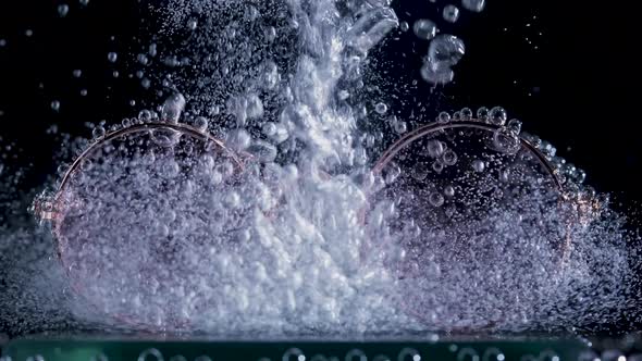 A Stream of Soda is Poured Into the Water Over Stylish Round Sunglasses Creating a Whirlwind of