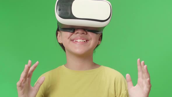 Excited Young Asian Kid Girl Using Virtual Reality Headset In Green Screen Studio