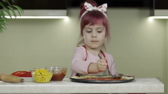 Cooking Pizza. Little Child in Apron Adding Tomato Sauce To Dough in Kitchen