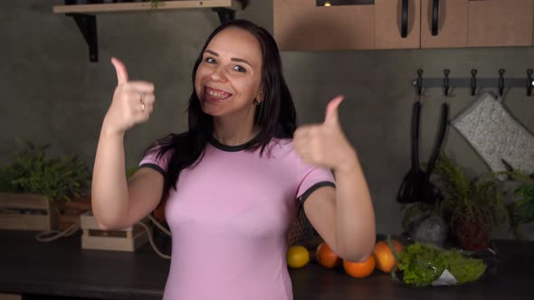 Young Woman Shows Thumbs Up Standing in Kitchen