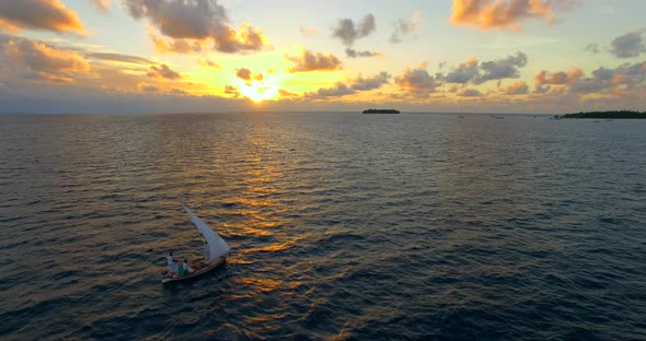 Aerial drone view of a man and woman sailing on a boat to a tropical island at sunset