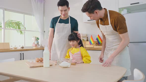 Asian attractive LGBTQ gay family teach girl kid kneads yeast dough bake bakery in kitchen at home.