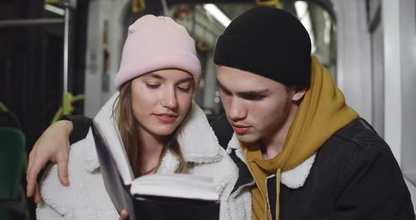 Young Couple Reading Book Together While Sitting in Bus. Lovely Guy Embracing His Girlfriend While