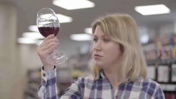 Side View of Concentrated Blond Caucasian Woman Looking at Red Wine in Glass. Professional Female