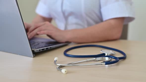 Female Doctor in a Medical Coat at the Desk Typing on a Laptop