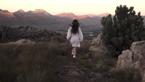 Unrecognizable woman running towards the mountains range in a rocky environment, slow motion freedom