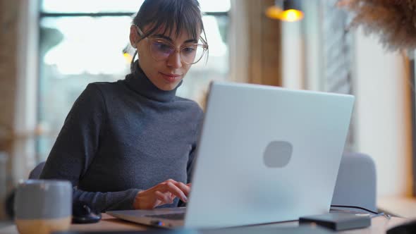 Portrait Young Woman in Eyeglasses Using Laptop in Coworking Space or Cafe and Drinking Coffe