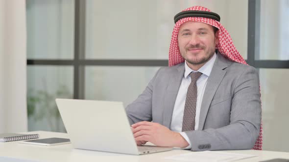 Middle Aged Arab Businessman Looking at Camera while using Laptop in Office