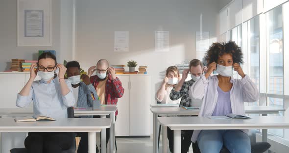 Multiethnic Young Students Putting on Face Mask Sitting at Desks at College