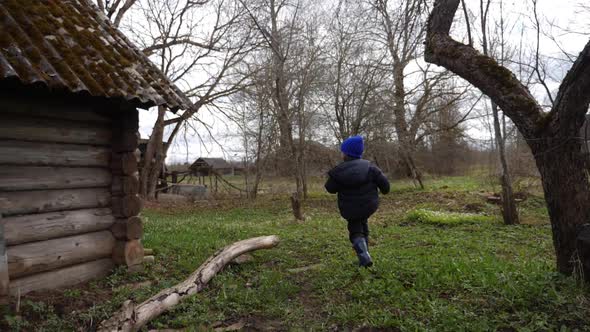 Boy Child in a Blue Hat Walks Through the Yard