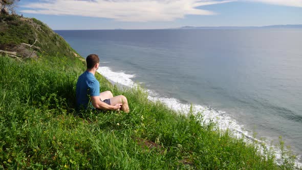 A man sitting in calming peace on the edge of a beach cliff in deep thought and meditation on a brig