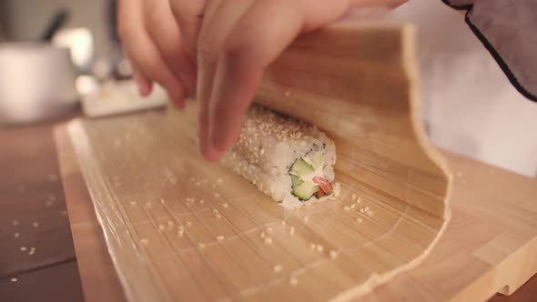 Hands of Man in Chef Clothing Prepare Sushi Roll of Japanese Cuisine with Sesame Seeds