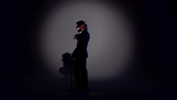 Elegant Man in a Black Hat Is Dancing an Erotic Dance. Spotlight on a Black Background