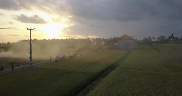 Aerial drone view of farming fields and a road with burning smoke at sunset.