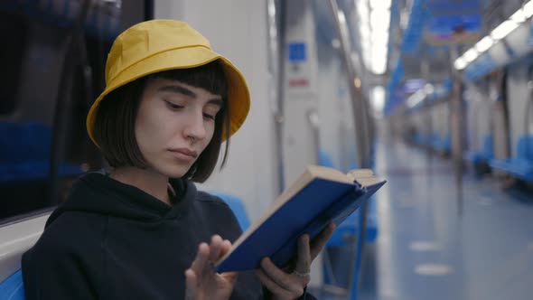 Young Woman Sitting at Subway Train and Reading Book