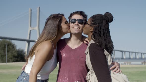 Two Female Friends Kissing Handsome Young Man on Meadow.