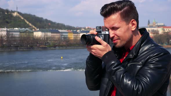 A Young Handsome Man Takes Photos with a Camera - Closeup - a River and a Quaint Townscape