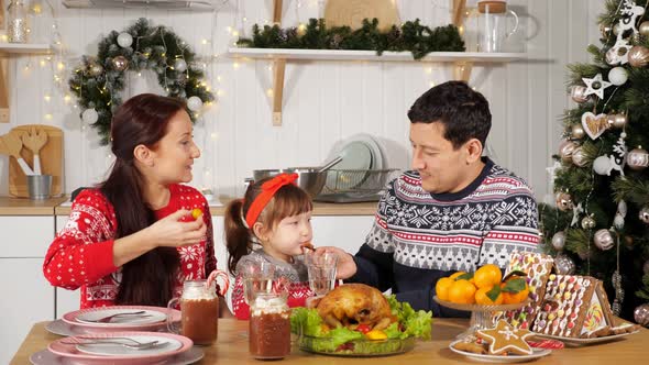 Father Feeds Daughter Sitting with Wife at Festive Table