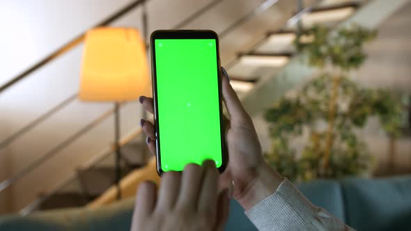 Chroma key mock-up on smartphone in hand. Woman holds mobile phone indoors of cozy home