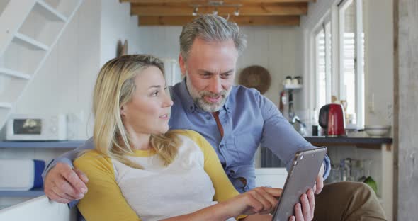 Happy caucasian mature couple using tablet and sitting in in living room