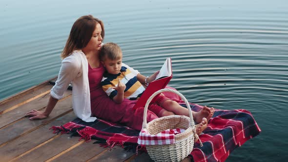 Mom Reads a Book To Little Son on the Lake