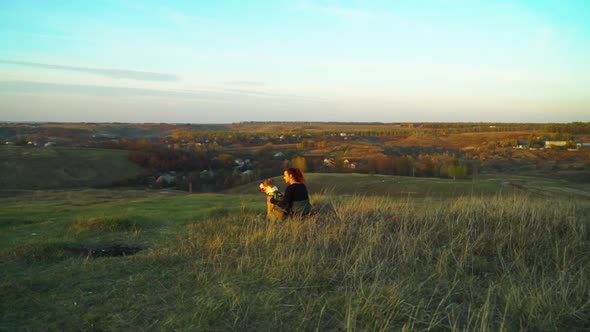 Owner and pet American Staffordshire terrier sitting on green hill at sunset