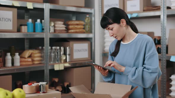 Woman with Checklist on Tablet Packing Donation Box