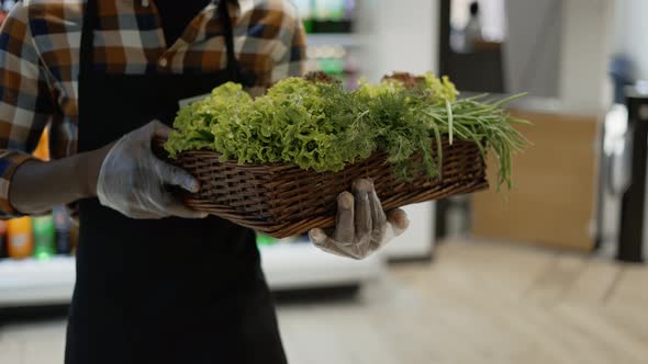Male Unrecognizable Worker in Gloves at the Store Walks with Basket Full of Greens