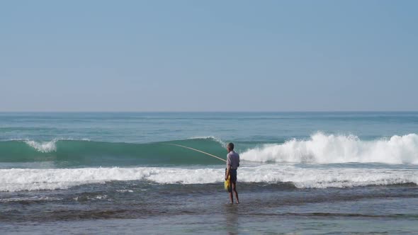 Local Fisherman Holds Rod in Hand in Waving Blue Ocean