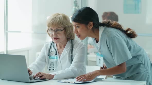 Hispanic Nurse and Senior Caucasian Doctor Using Laptop and Speaking