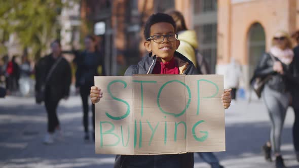 Portrait of African Preteen Boy Standing Outdoors School Building with Stop Bullying Cardboard Sign