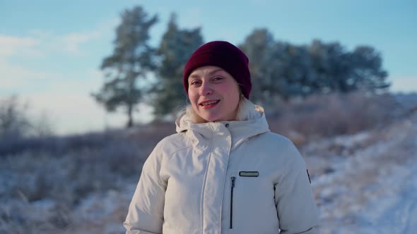 Portrait female person standing at winter forest outdoors. Attractive woman looking at camera