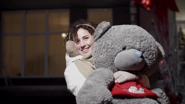 Smiling Woman Hugging Huge Teddy Bear Outdoors at Night