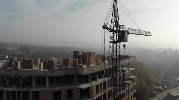 Birds eye view on tower crane in fog standing next to residential building.