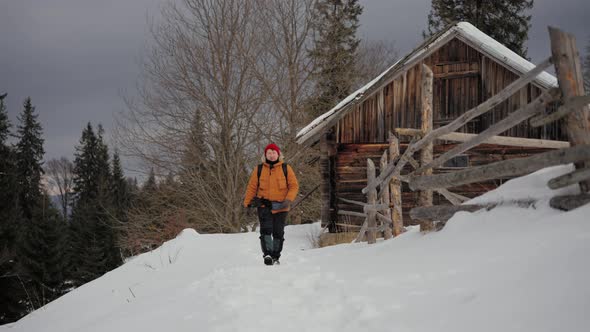 Walking Tourist Man Equipped Through the Snow to Amazing Wooden House in Countryside in the Middle