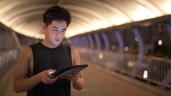 Portrait of Young Handsome Asian Man Thinking While Using Digital Tablet Outdoors at Night
