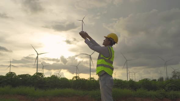 Portrait of Asian windmill engineer man, worker working, holding a model on site at wind turbines