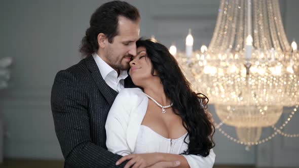 the Groom Hugs the Bride From Behind and Touches Her Long Hair Against the Background of a Crystal