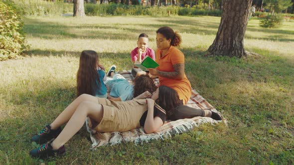 School Teacher Reading Book to Mixed Race Elementary Students Outdoors