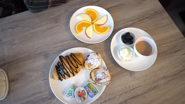 Top view of breakfast on table. Tea with lemon, pastries, croissant and fruit.