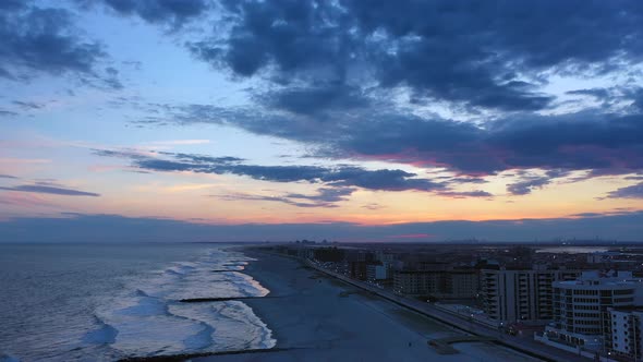 A drone shot over a quiet beach during sunset. The camera dolly out and boom down over the shore whi