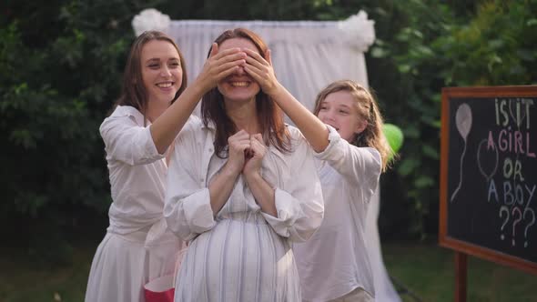 Surprised Pregnant Caucasian Woman Standing on Backyard As Daughters Covering Eyes with Hands