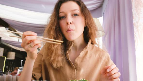 Beautiful Caucasian Girl Appetizing To Eat Rolls with Chopsticks in a Japanese Restaurant