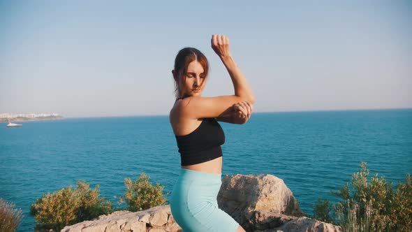 Sportive Woman Stands on the Hill By the Sea and Stretching Her Hands