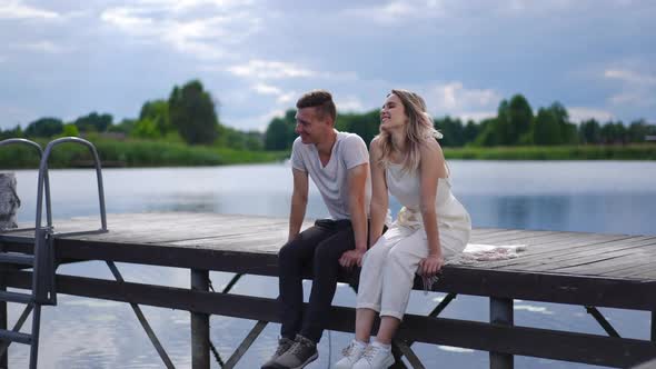 Happy Carefree Young Couple Sitting on Wooden Pier Talking Smiling Dating Outdoors