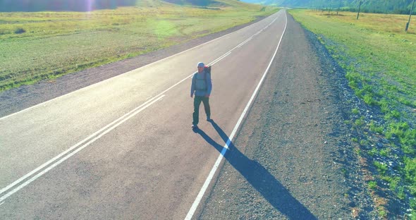 Flight Over Hitchhiker Tourist Walking on Asphalt Road. Huge Rural Valley at Summer Day